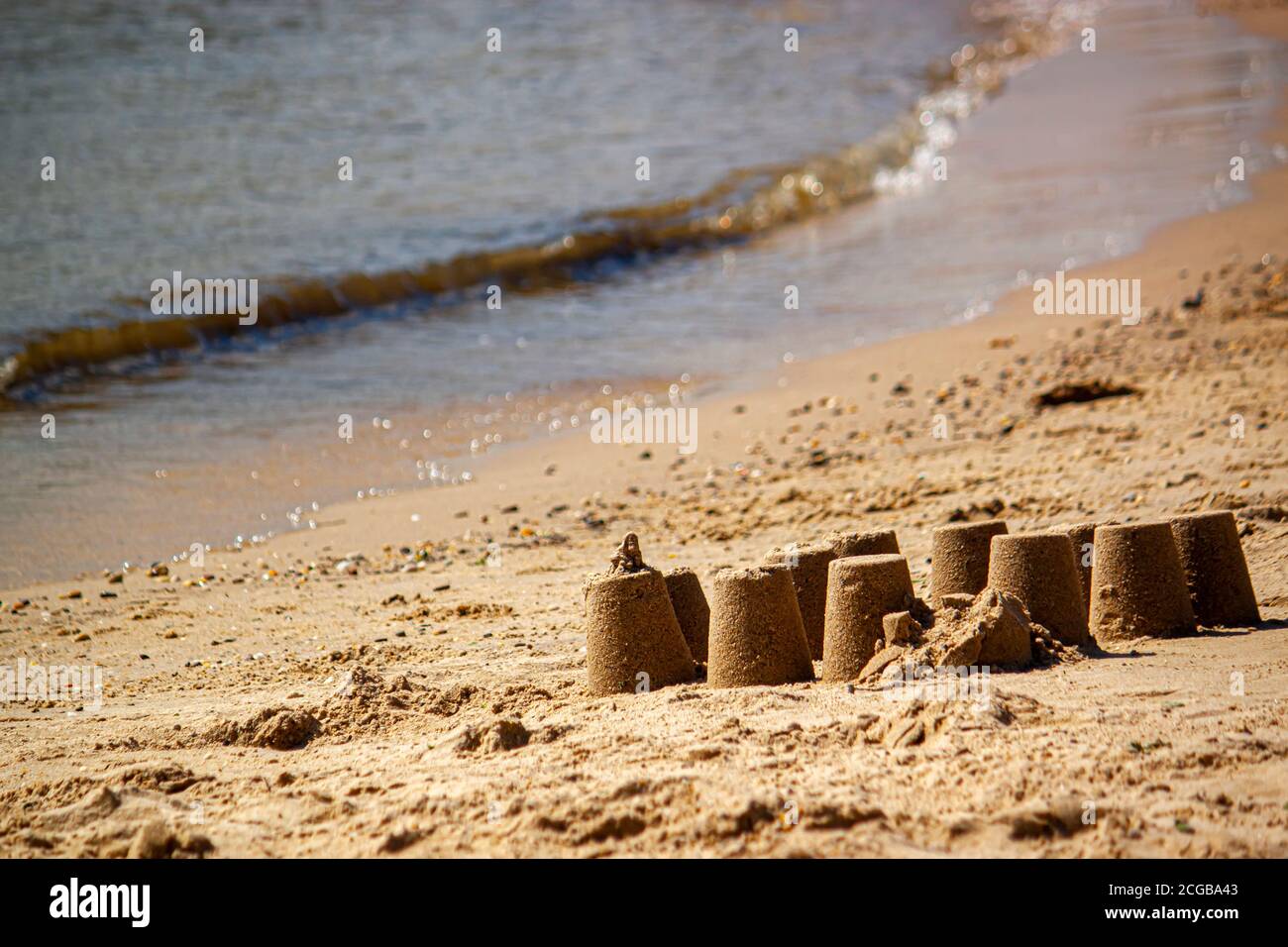 Un'immagine astratta a tema per le vacanze in spiaggia con un'occhiata da vicino a un castello di sabbia fatto di sabbia bagnata su una spiaggia. Non c'è nessuno e il mare calmo è nel Th Foto Stock