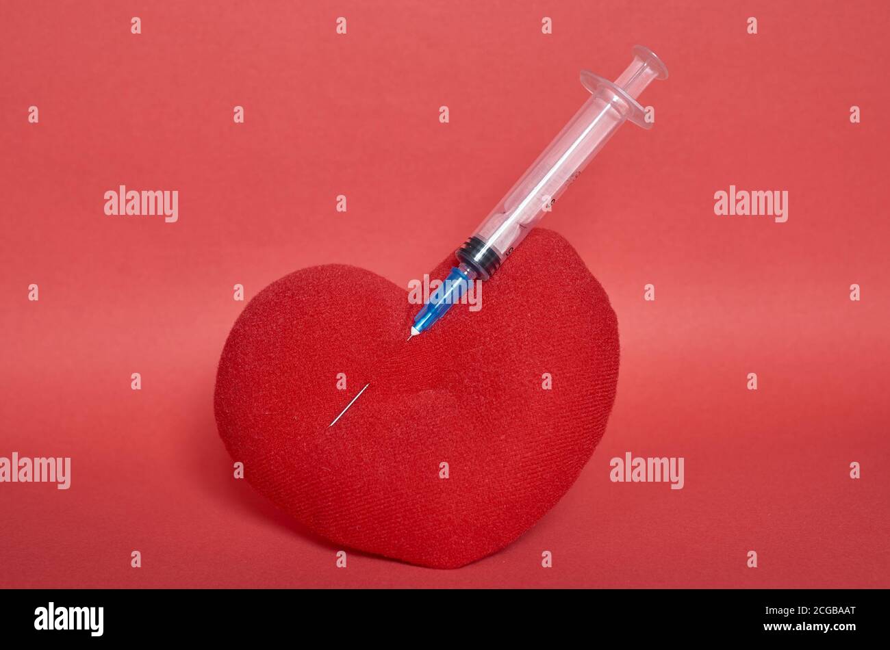 Un cuore giocattolo imbottito con una siringa bloccata in esso. Sfondo rosso. Formato verticale Foto Stock