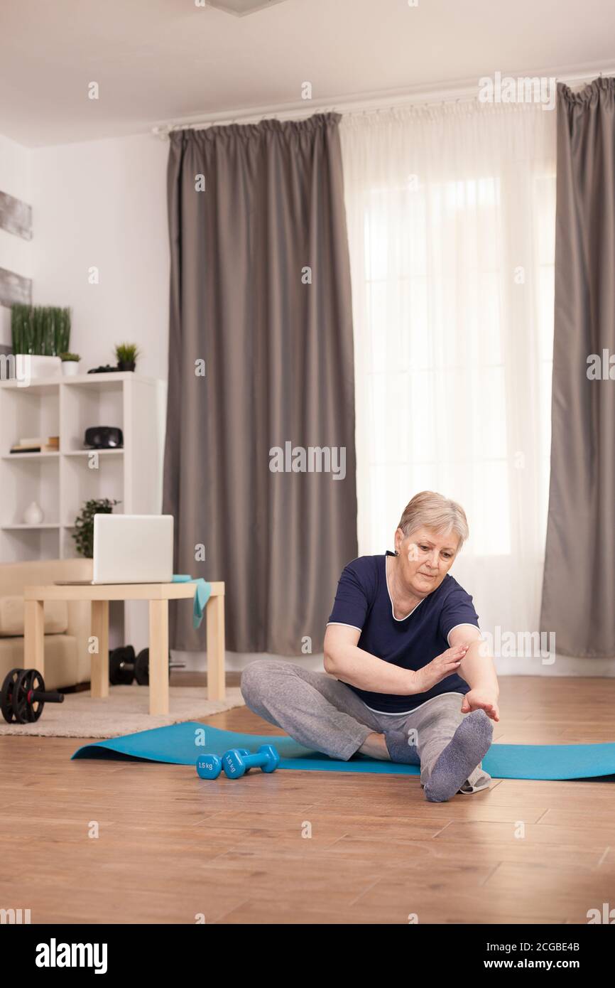 Nonna con uno stile di vita healty facendo formazione streching. Anziano pensionato online internet esercizio di formazione a casa attività sportiva con manubri, banda di resistenza, palla svizzera all'età di anziano pensionamento Foto Stock