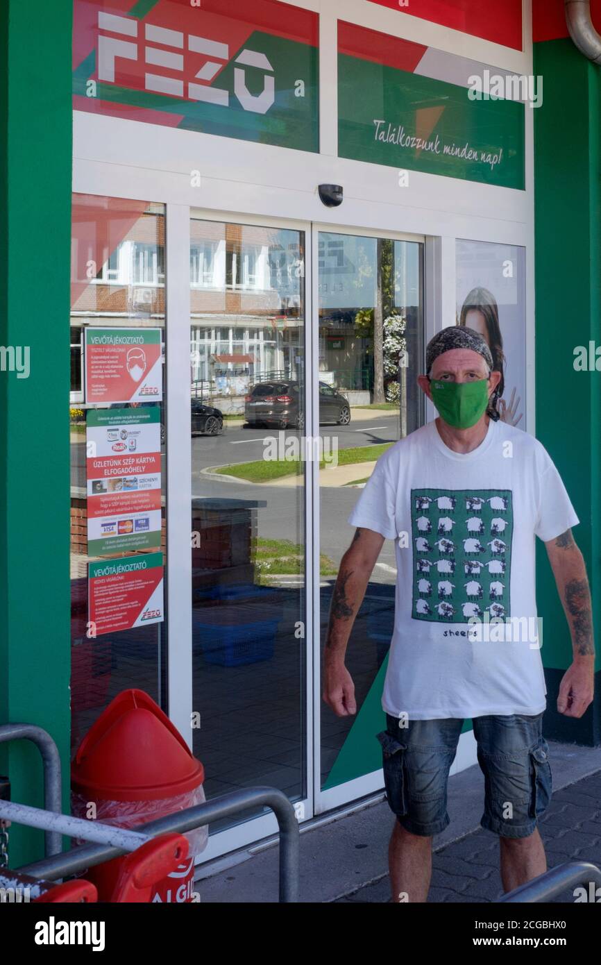 uomo più anziano mascherato in piedi fuori del supermercato che indossa t.shirt di pecora in protesta passiva contro l'uso forzato della maschera viso lenti contea di zala ungheria Foto Stock