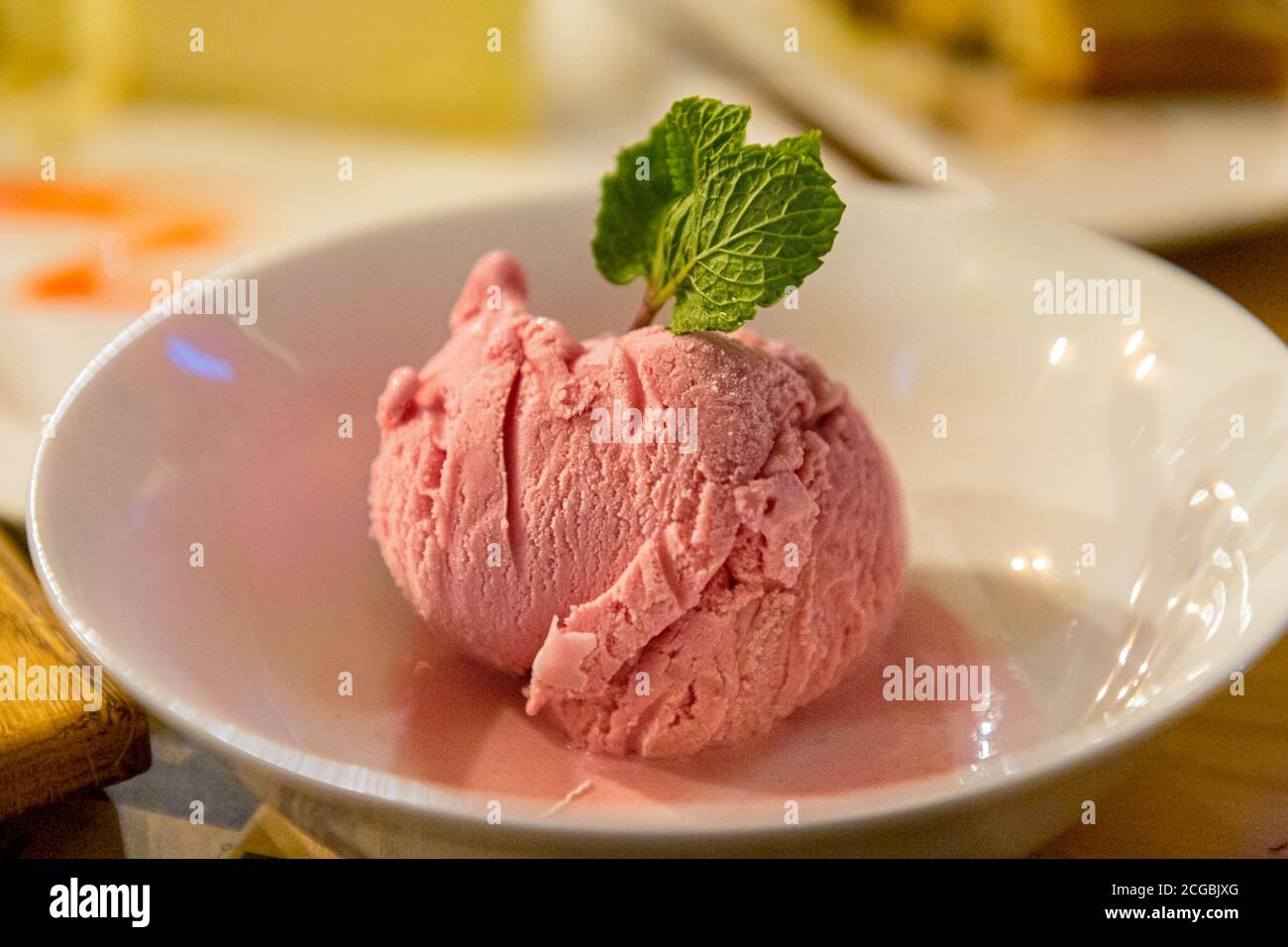 Una palla di gelato alla fragola con una foglia di menta è sul piatto. Foto Stock