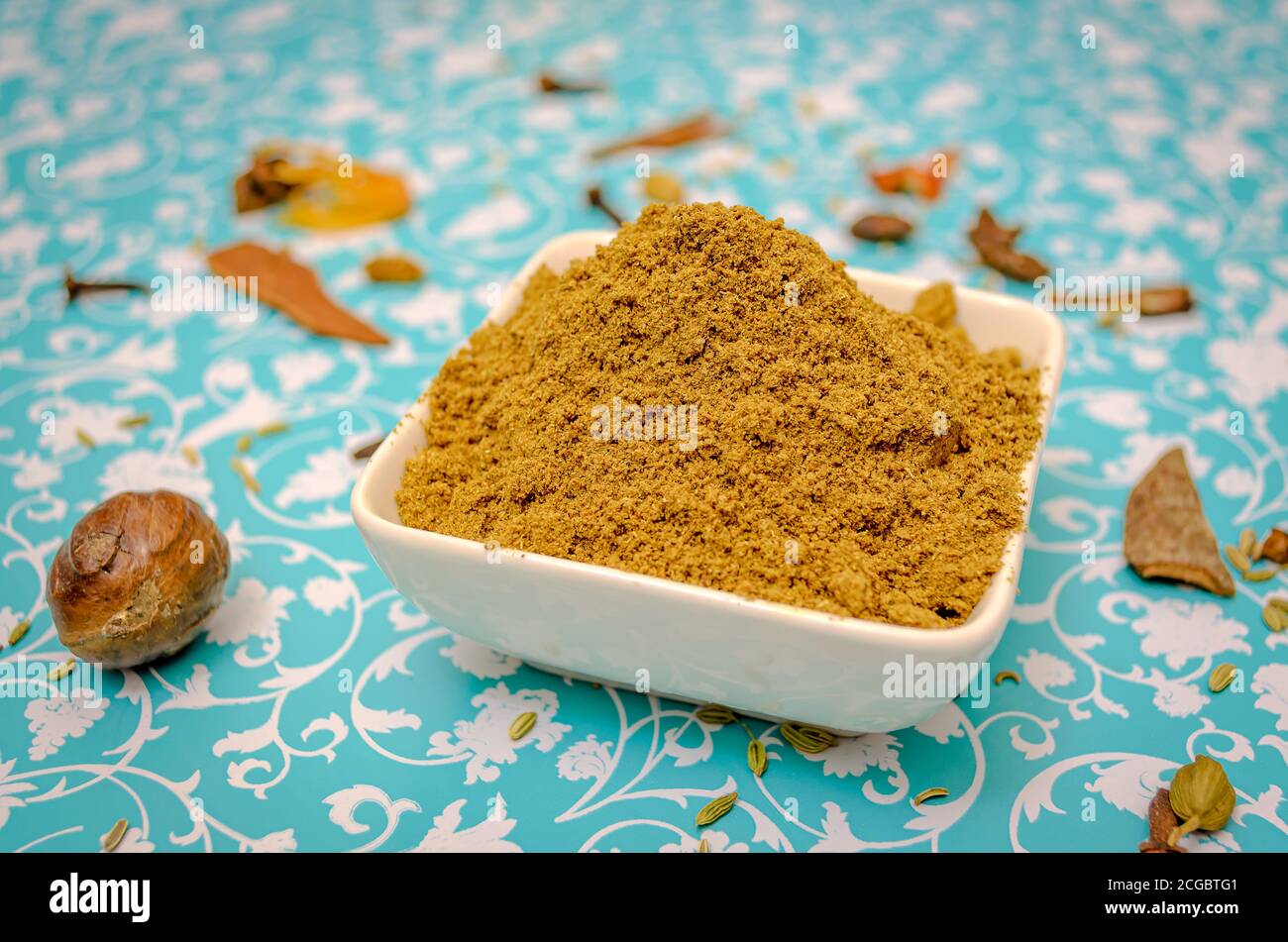 Primo piano di Garam Masala polvere in una ciotola su un tavolo di sfondo floreale con spezie come sostegno Foto Stock