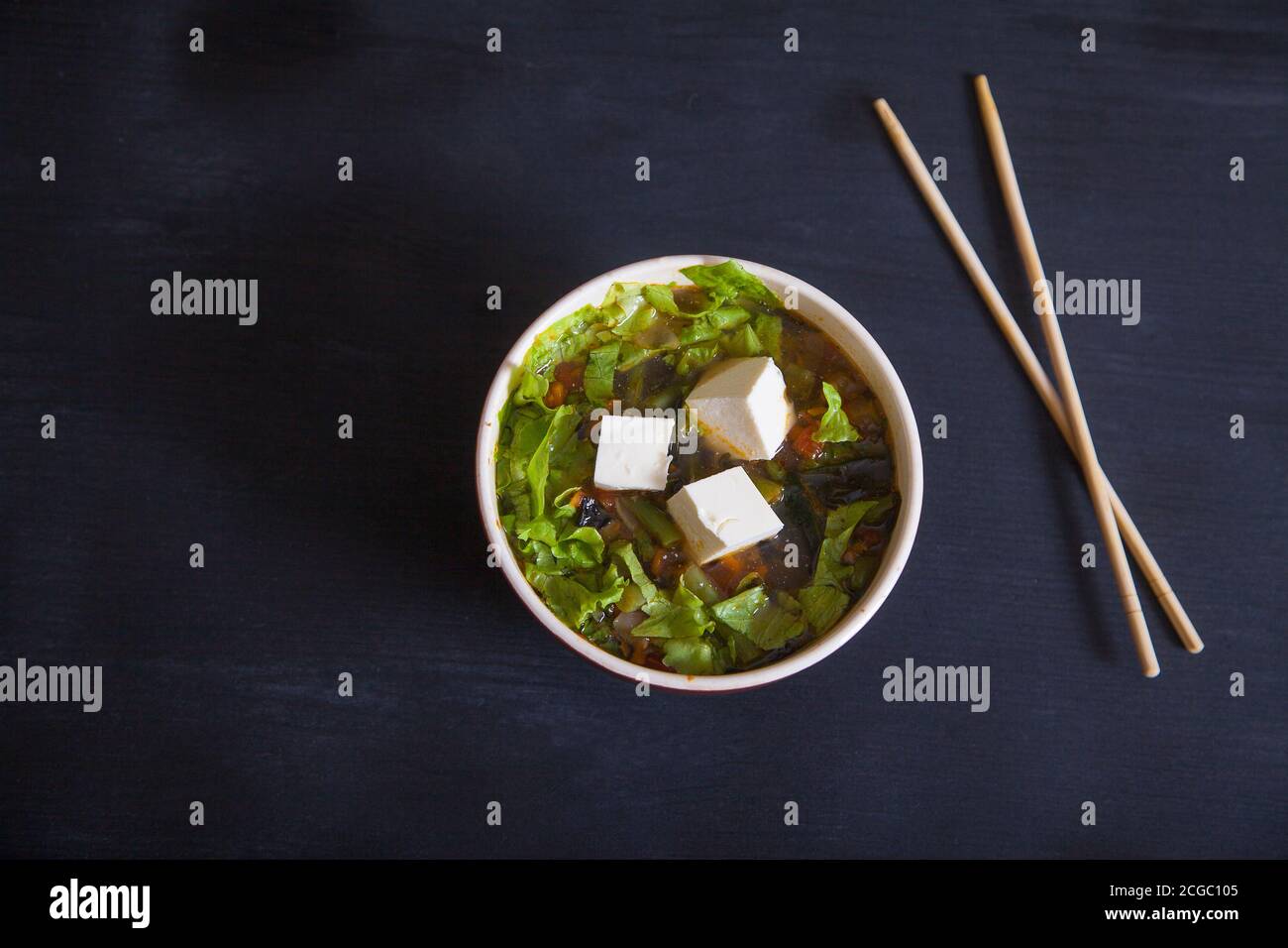 Zuppa giapponese con formaggio tofu, fagioli verdi, verdure, erbe, bastoncini di bambù su sfondo nero. Copia spaes Foto Stock