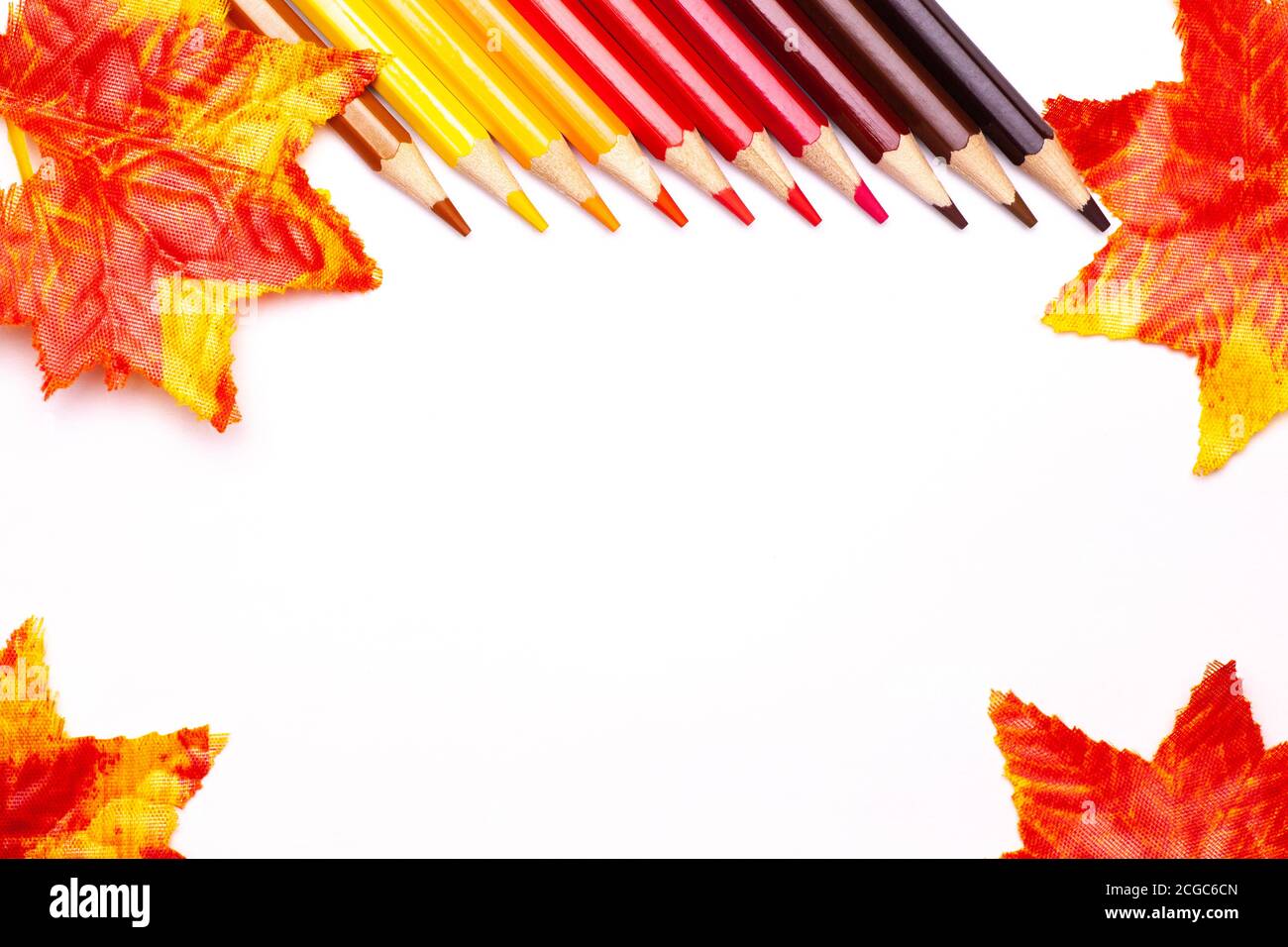 matite di legno multicolore in tonalità rosse su un bianco isolato sfondo e foglie di autunno arancio Foto Stock