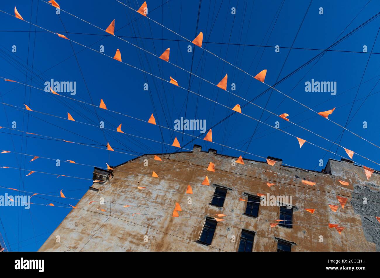 Molte bandiere arancioni sui fili contro il cielo blu e il bordo di una vecchia casa abbandonata Foto Stock