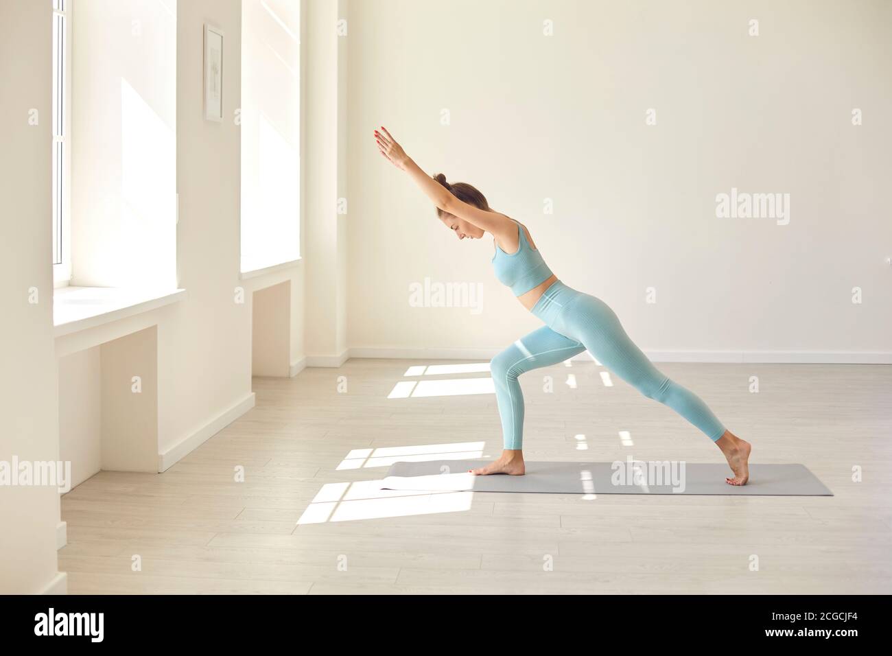 Donna giovane seria che pratica l'equilibratura asana in piedi sul tappetino di gomma durante l'allenamento yoga in palestra Foto Stock