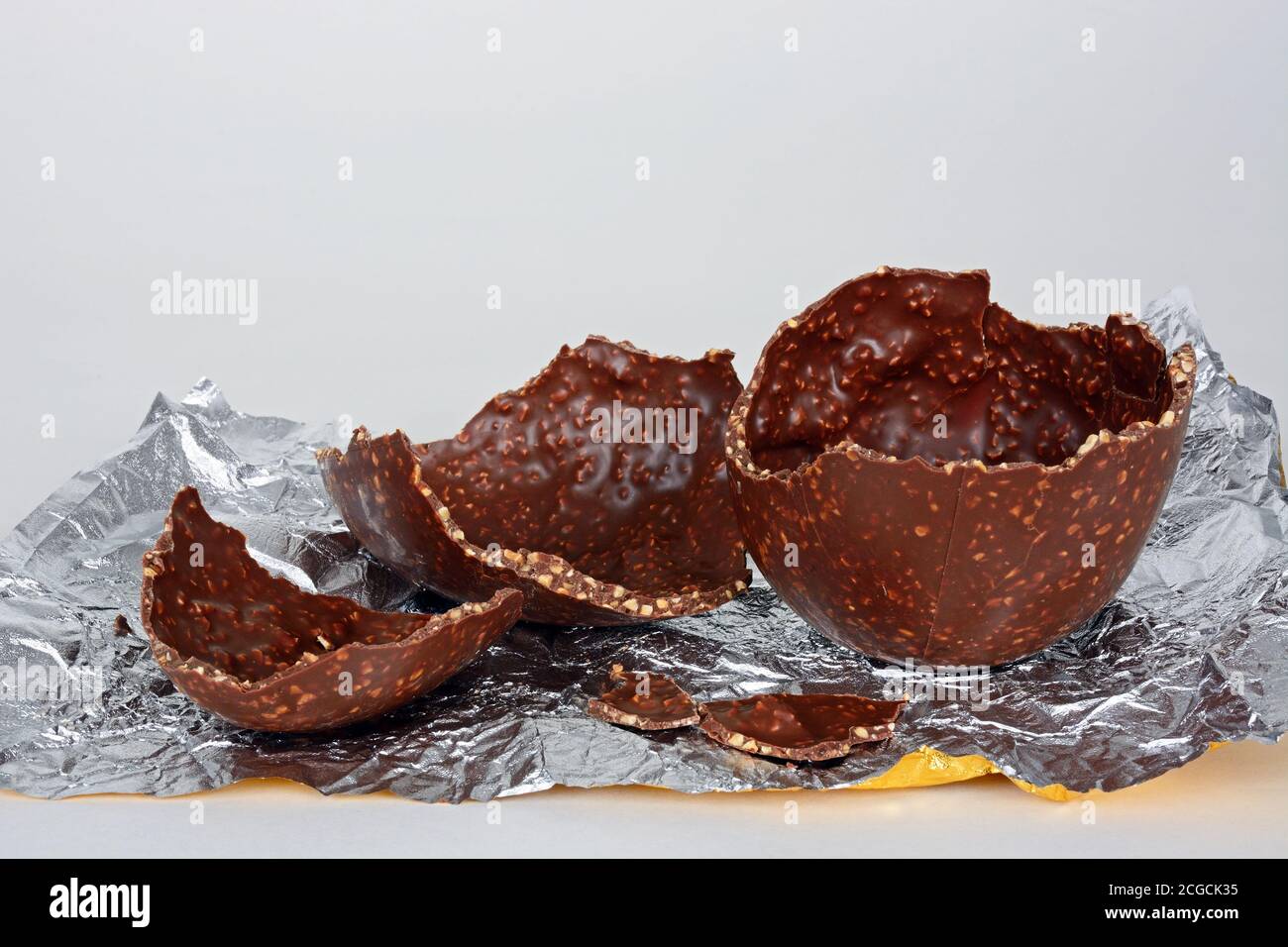 Uovo di Pasqua al cioccolato rotto con nocciole tritate su un foglio di foglio di alluminio su sfondo bianco, Regno Unito. Foto Stock