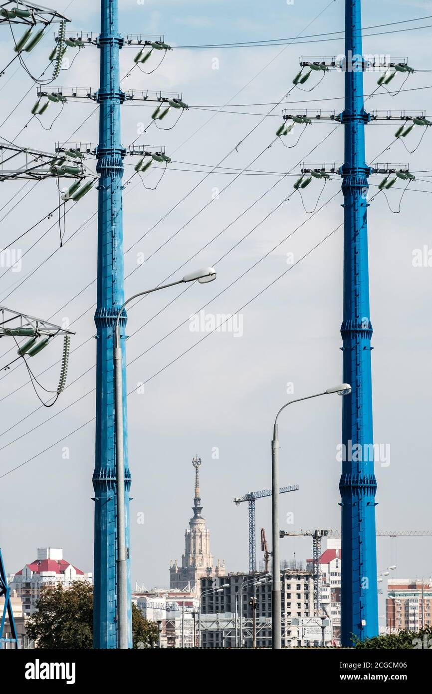 Due montanti blu ad alta tensione che formano una struttura naturale sullo sfondo degli edifici urbani. Fili e isolatori. Foto Stock