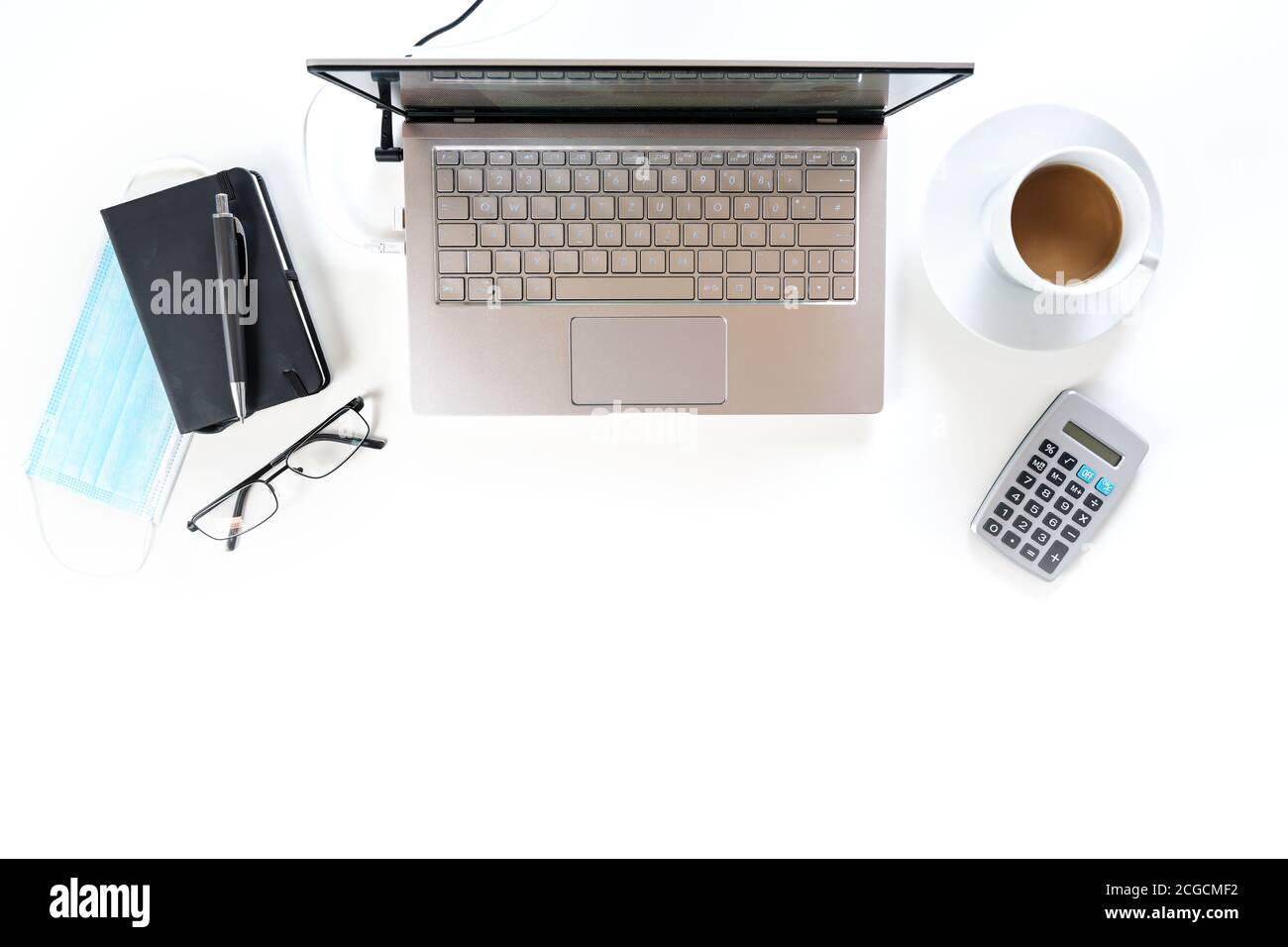 Scrivania da ufficio bianca con computer portatile, utilità di lavoro e una maschera chirurgica contro il coronavirus e covid-19 infezione, nuova attività normale, spazio di copia, alto Foto Stock