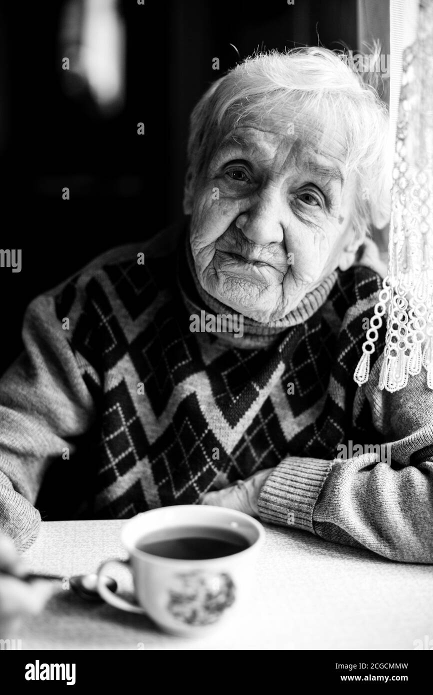 Un ritratto di donna anziana seduto al tavolo nel maglione. Foto in bianco e nero. Foto Stock