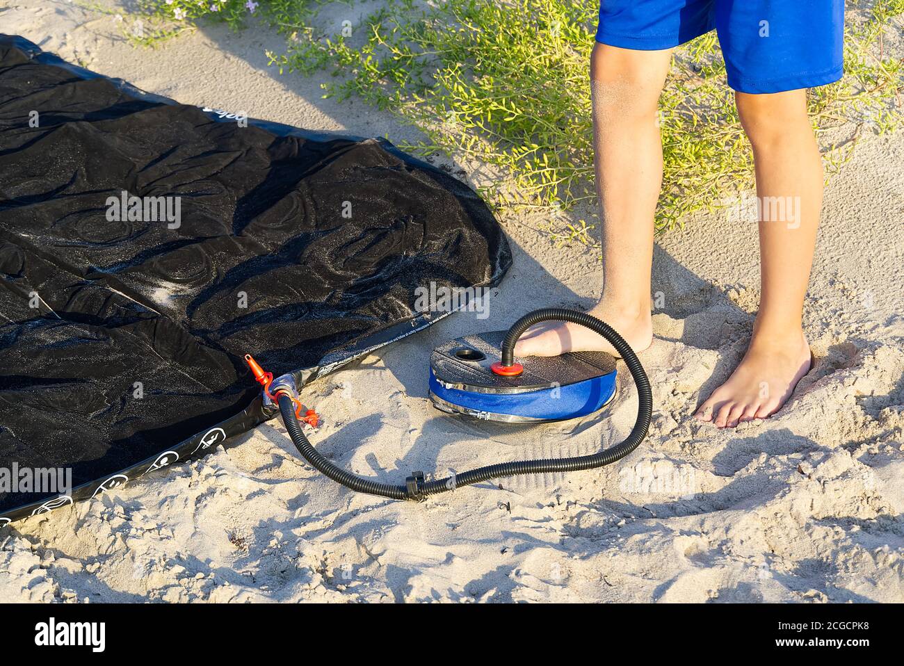 Un uomo con pompa aria a pedale pompa un materasso gonfiabile o letto d'aria sulla spiaggia di sabbia. Il piede gonfia il materasso ad aria con la pompa a pedale sulla sabbia. Foto Stock
