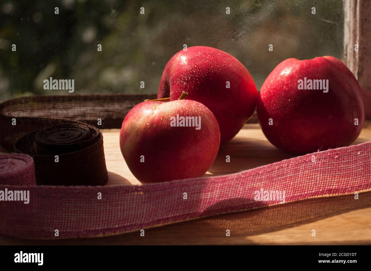 Mele rosse da vicino, luce dura, cibo vegetariano. Raccolta. Tre mele sulla finestra di fronte al vetro, luce solare intensa Foto Stock