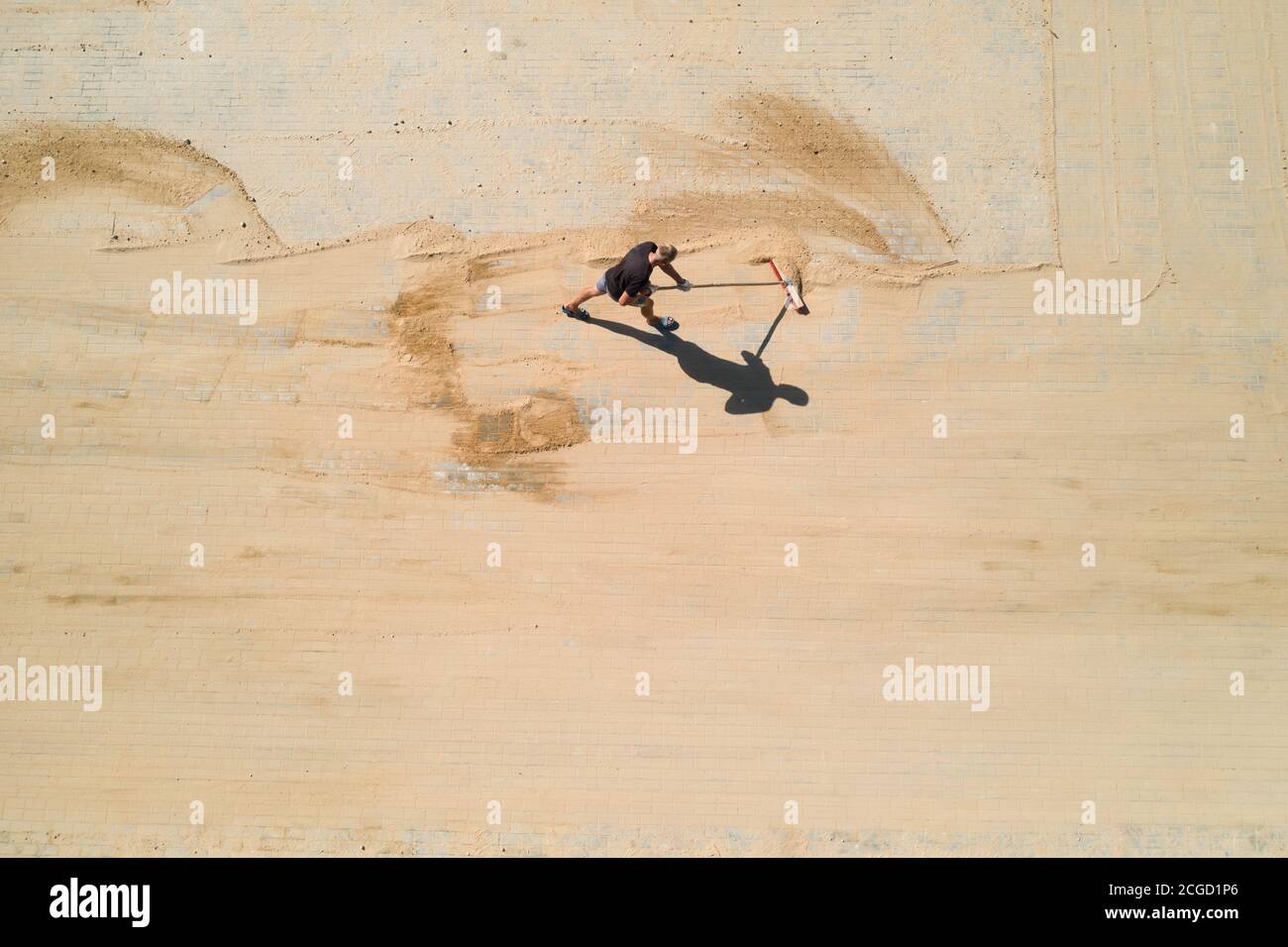 il lavoratore spazza la sabbia nei giunti delle lastre di pavimentazione vista dall'alto. Foto Stock