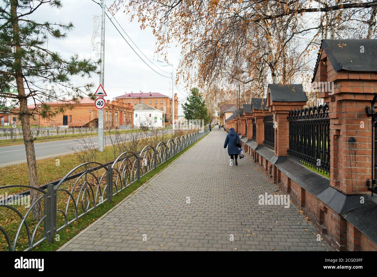 Una donna cammina lungo il marciapiede davanti a una vecchia recinzione lungo Lenin Street, nel centro storico di Yeniseisk. Regione di Krasnoyarsk. Russia. Foto Stock