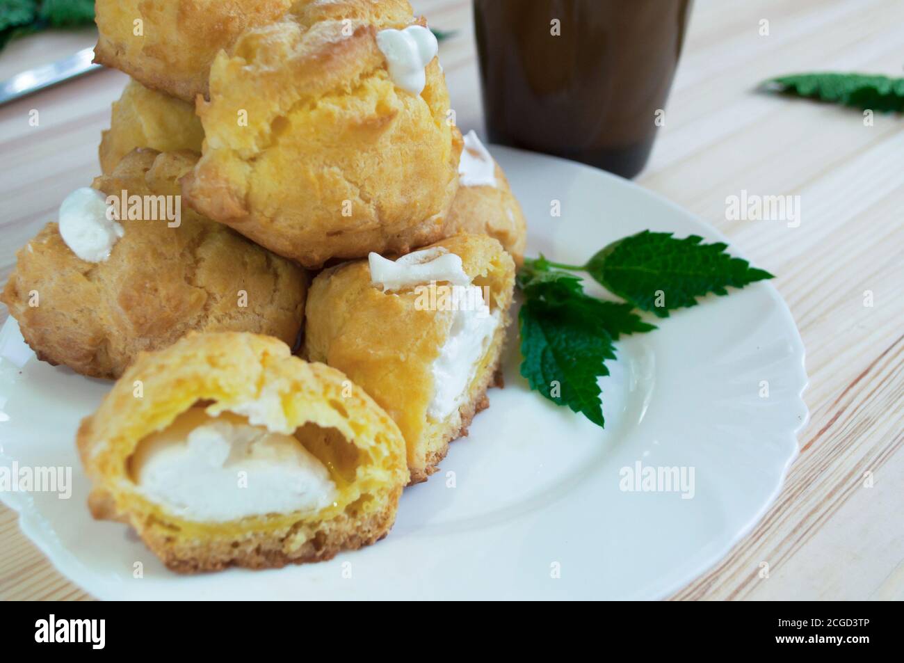 Porzione di eclair ripiena di panna montata con una tazza di caffè con latte su fondo di legno. Impilare i biscotti per la crema. Eclairs su un whi Foto Stock