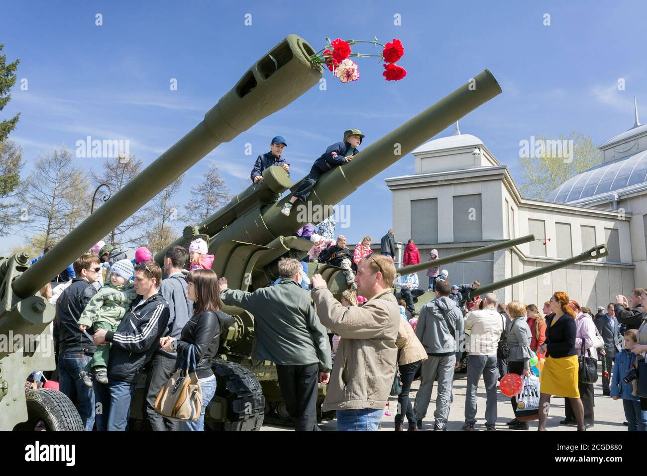 I bambini salgono sulle pistole di artiglieria, esposte vicino al museo della costruzione del Memoriale della Vittoria durante la celebrazione della Giornata della Vittoria della seconda Guerra Mondiale. Krasnoyarsk. Foto Stock