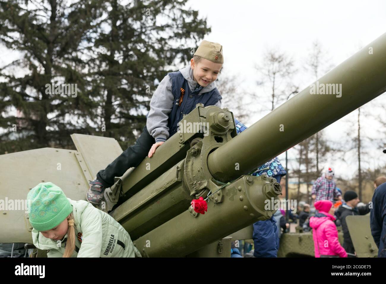 Il ragazzo è seduto sulla pistola d'artiglieria, che si trova vicino al museo della Vittoria Memorial durante la celebrazione della vittoria Giornata della seconda guerra mondiale. Krasnoyarsk. Foto Stock
