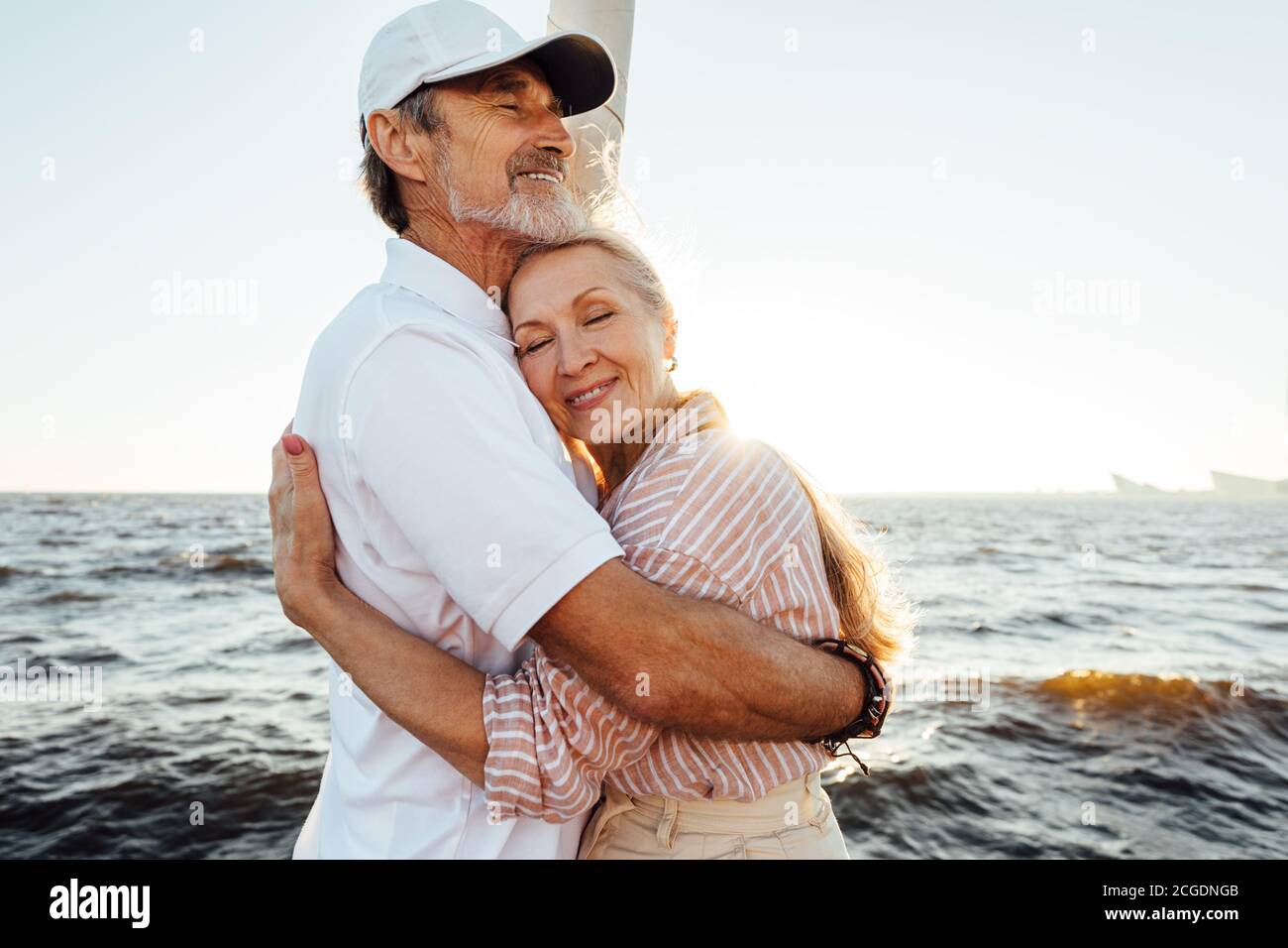 Affettuosa coppia senior abbracciando su yacht privato. Bella donna matura appoggiata sul petto del marito con gli occhi chiusi. Foto Stock