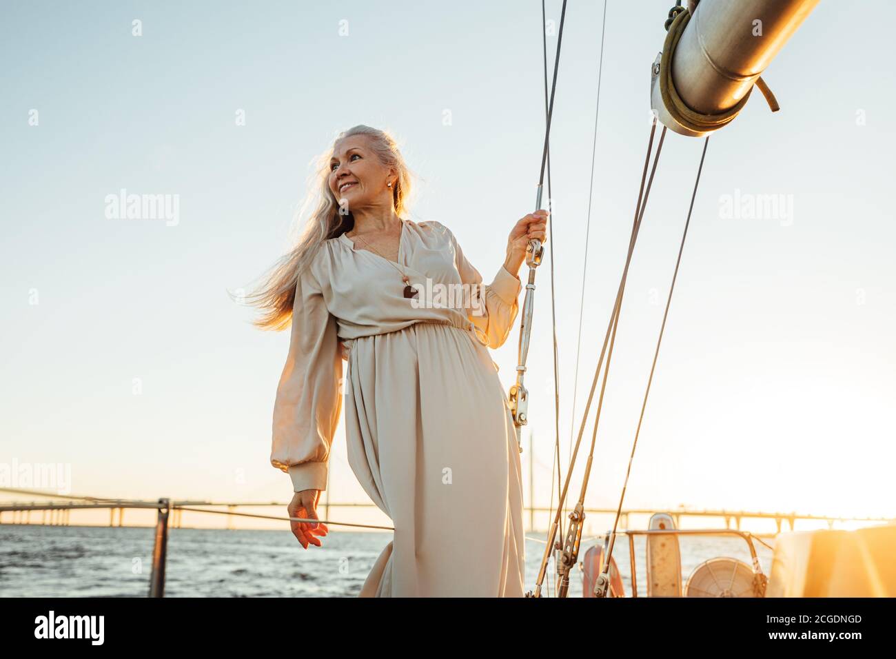 Bella donna senior in abito lungo guardando lontano all'aperto. Donna caucasica matura in piedi su un ponte barca a vela. Foto Stock