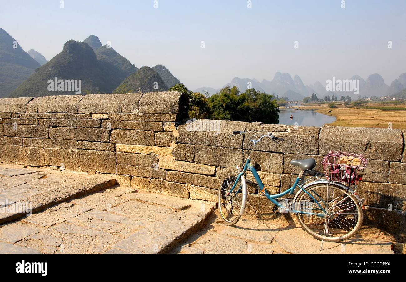 Scenario lungo il fiume Yulong vicino Yangshuo, Guilin nella provincia di Guangxi, Cina. Una bicicletta su un ponte di pietra che attraversa il fiume Yulong Foto Stock
