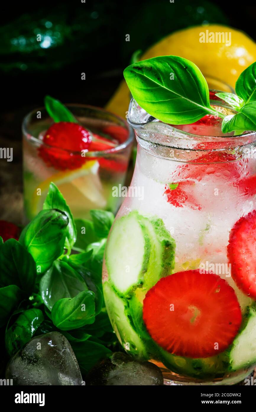 Limonata al basilico di cetrioli con fragole e ghiaccio in una caraffa, sfondo di legno vintage, fuoco selettivo Foto Stock