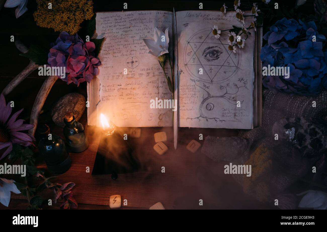 Apri il vecchio libro con incantesimi magici, rune, candela nera ed erbe sulla tavola delle streghe. Concetto occulto, esoterico, divinazione e wicca. Halloween vintage backg Foto Stock
