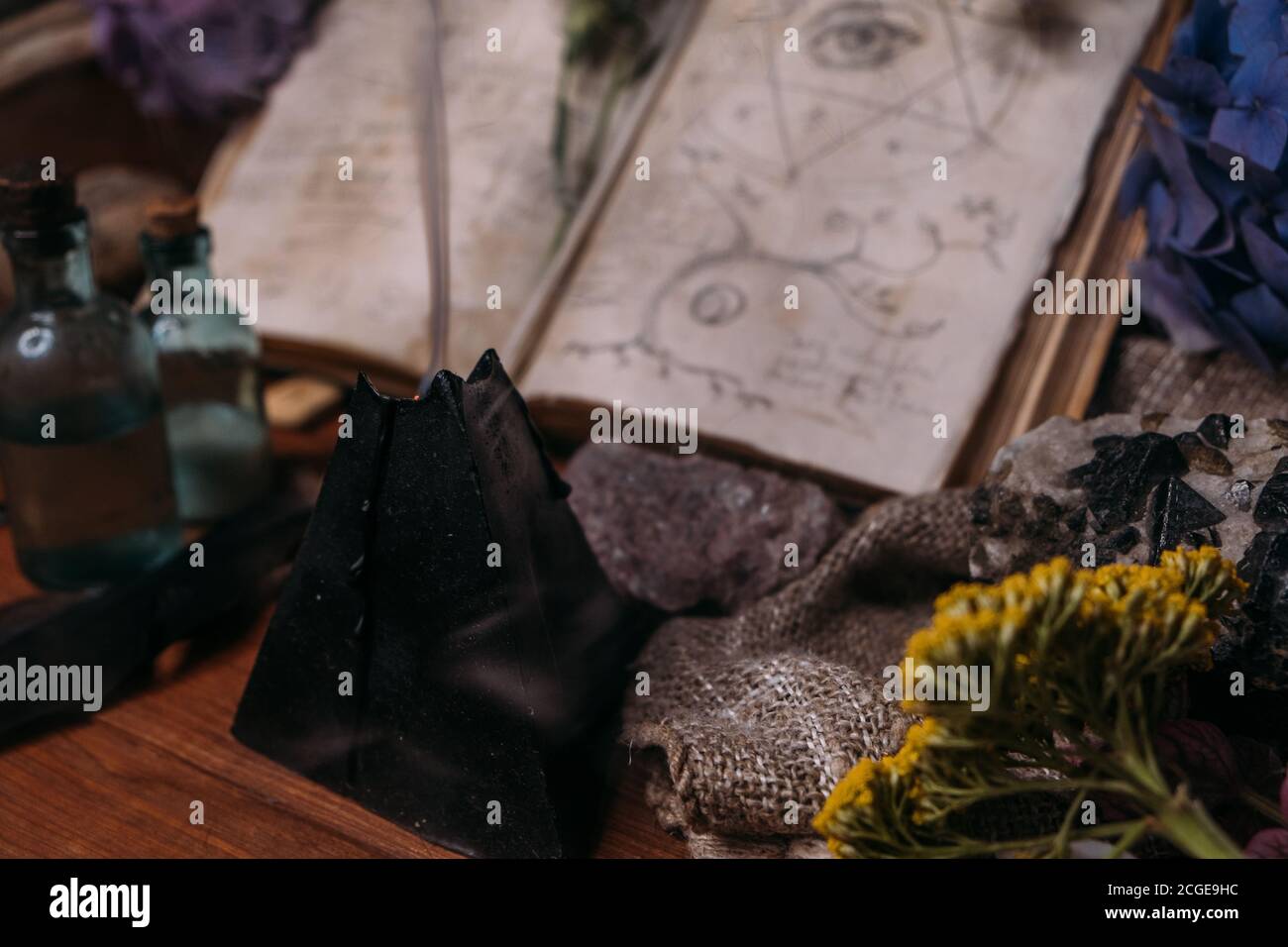 Apri il vecchio libro con incantesimi magici, rune, candela nera ed erbe sulla tavola delle streghe. Concetto occulto, esoterico, divinazione e wicca. Halloween vintage backg Foto Stock