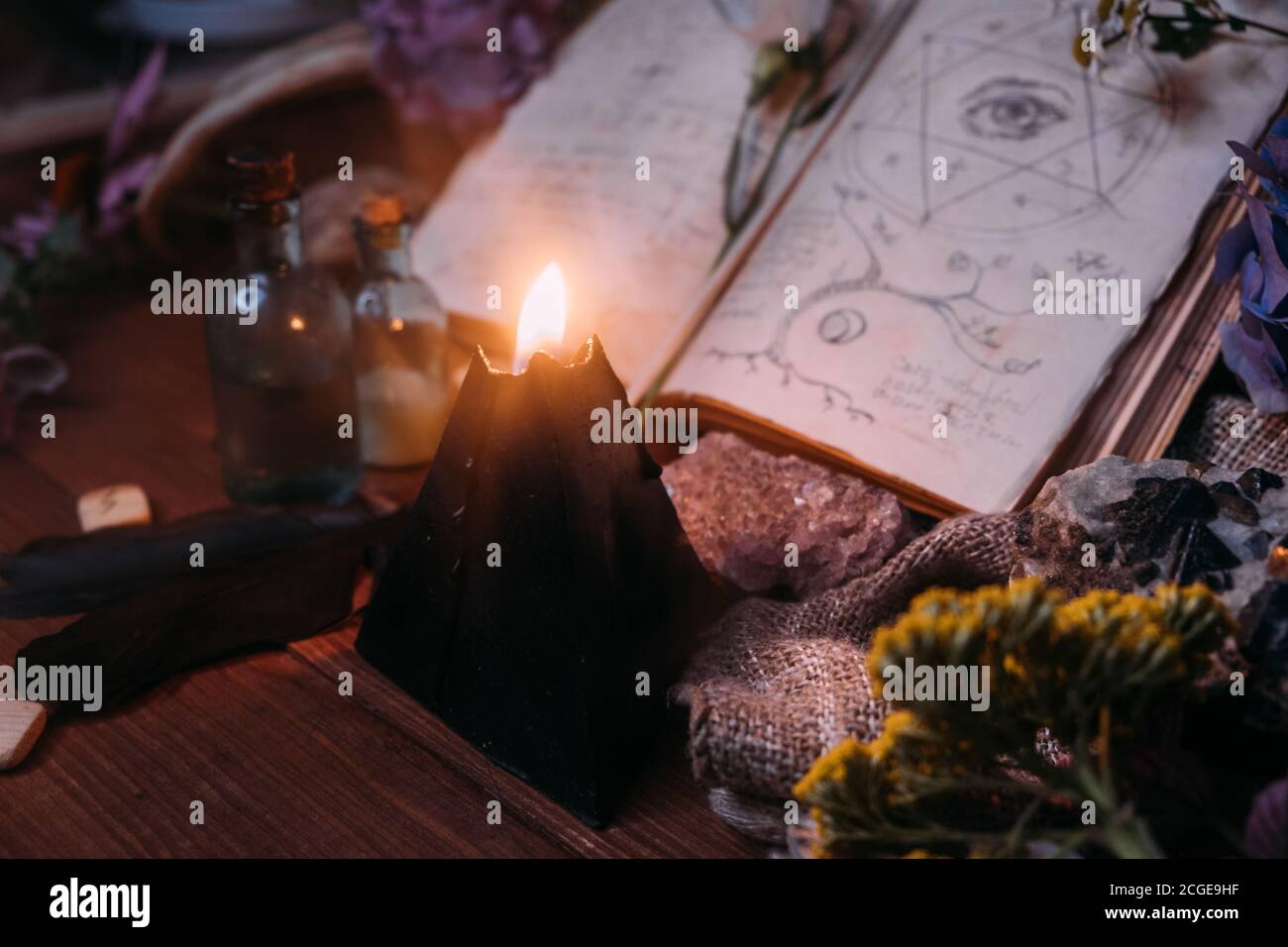 Apri il vecchio libro con incantesimi magici, rune, candela nera ed erbe sulla tavola delle streghe. Concetto occulto, esoterico, divinazione e wicca. Halloween vintage backg Foto Stock