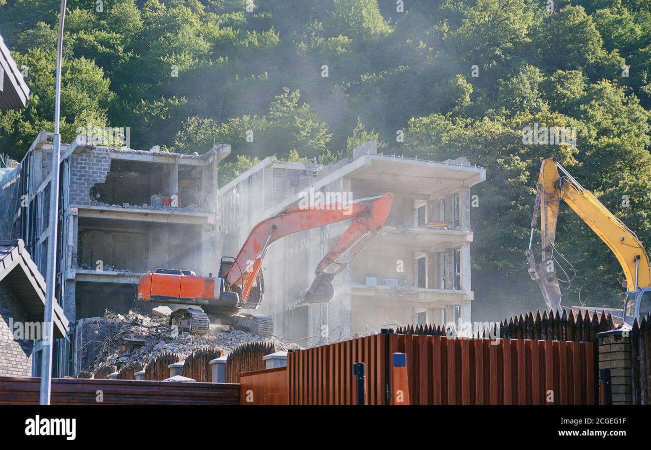 Il grande escavatore giallo rompe la vecchia casa in estate Foto Stock