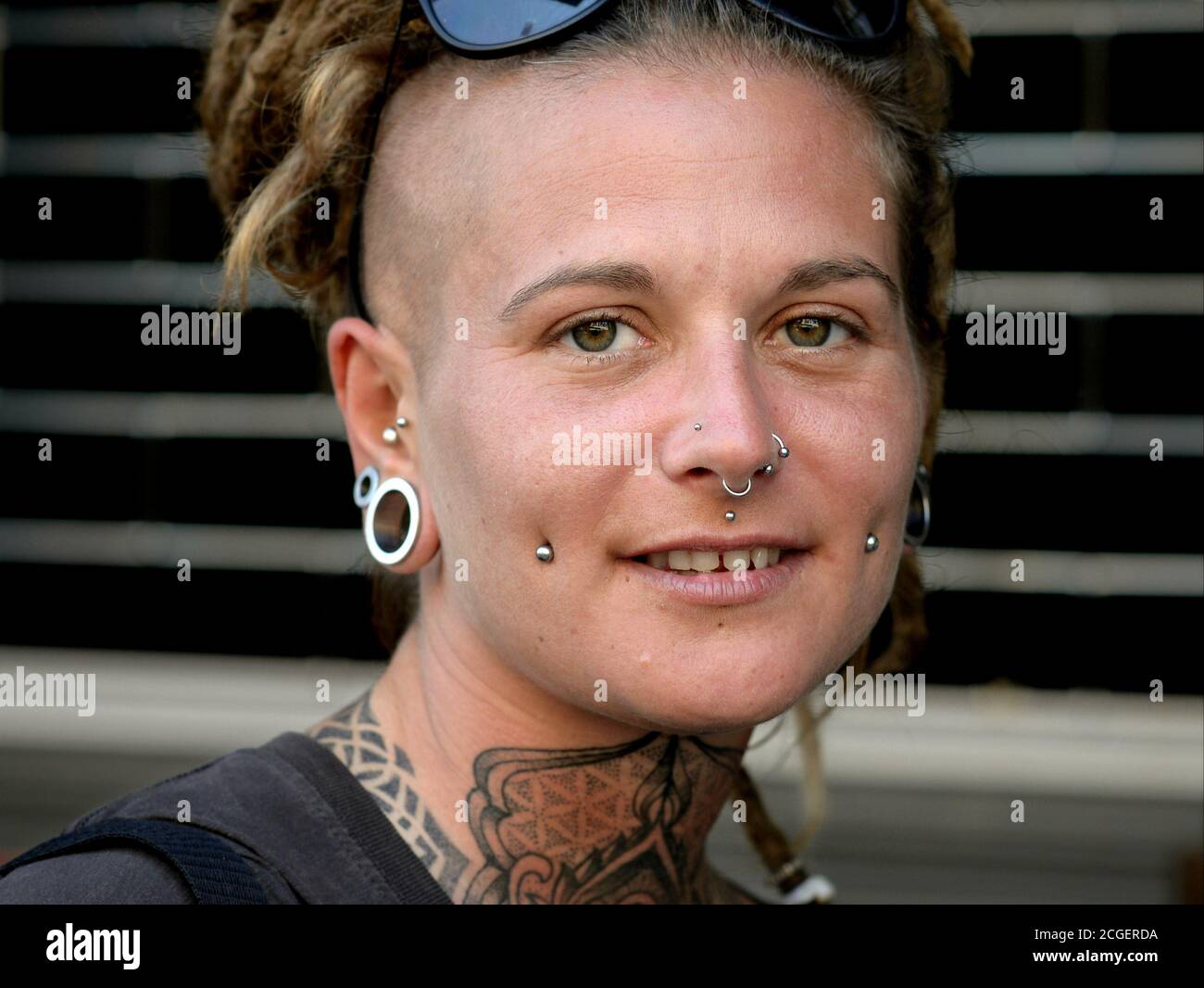 Giovane donna caucasica con piercing viso, tatuaggi e dreadlock pone per la macchina fotografica. Foto Stock