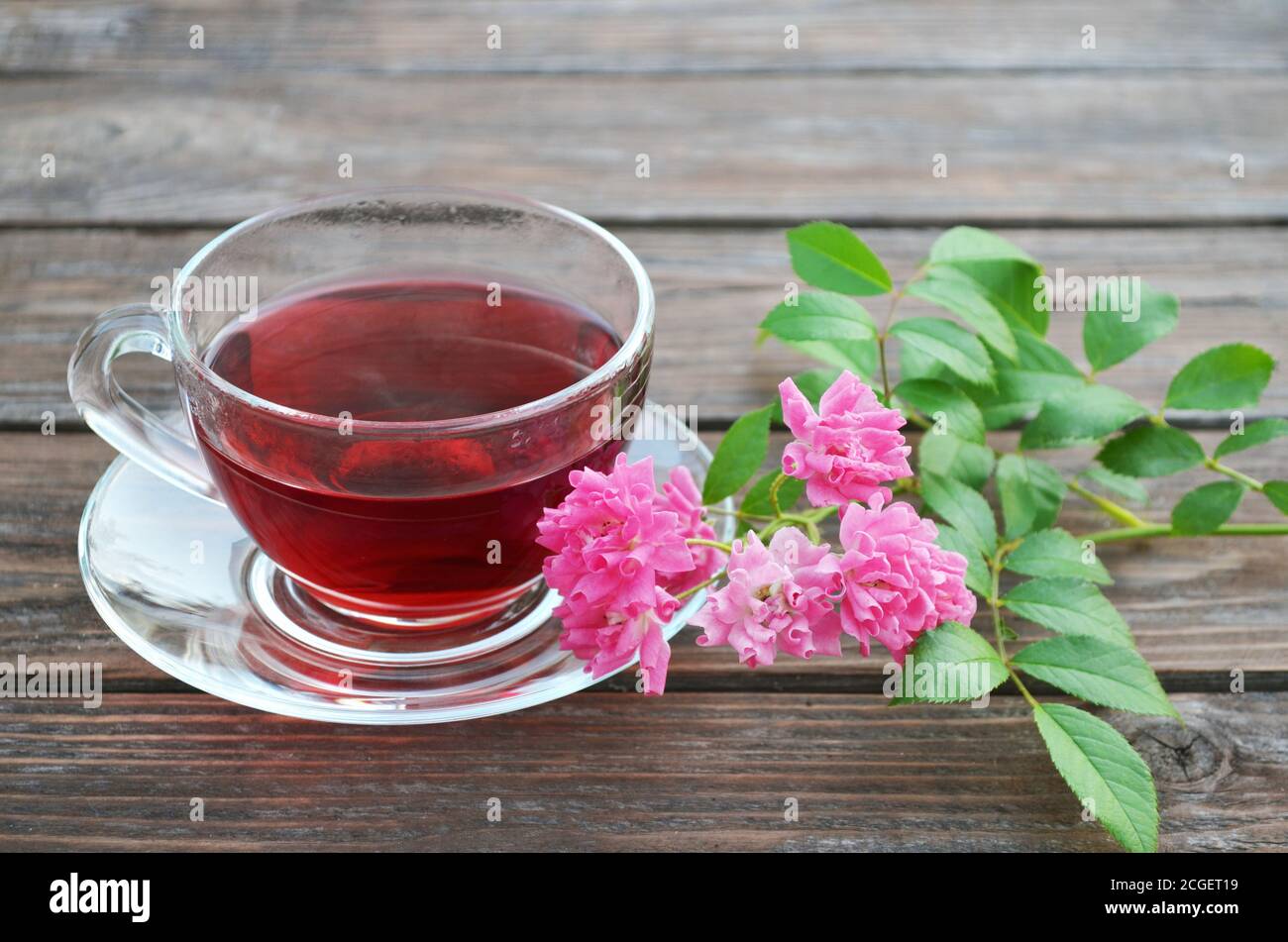 Tazza di tè caldo appena fatto e rose rosa su un vecchio tavolo di legno. Foto Stock
