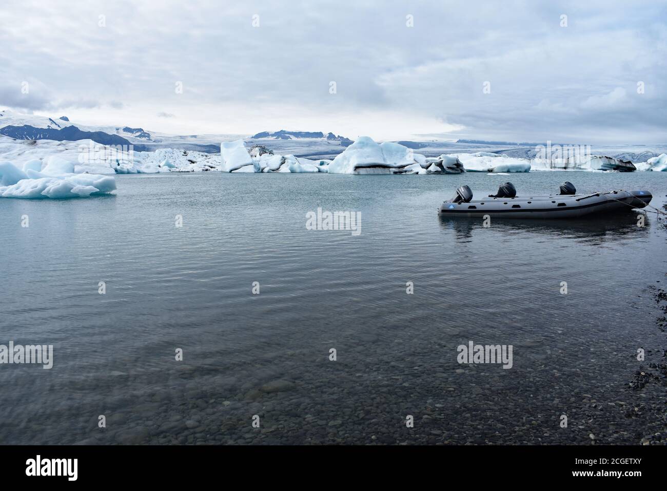 Una barca zodiaca legata nelle acque poco profonde sul lato del lago della Laguna del Ghiacciaio di Jökulsárlón, Islanda del Sud. Gli iceberg galleggiano dietro Foto Stock