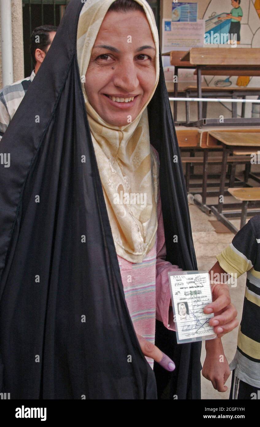Una donna irachena, vestito in abbigliamento personalizzato, ha il suo dito inchiostrato dopo la colata di una votazione sul referendum costituzionale in corrispondenza di una stazione di polling. Essa visualizza il suo ID utilizzato durante la votazione. Foto Stock