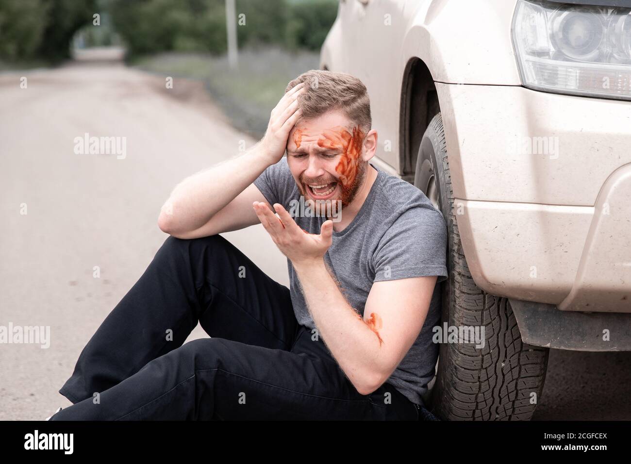 Incidente d'auto, l'uomo si siede con testa sanguinosa vicino ruota, urlando e piangendo Foto Stock