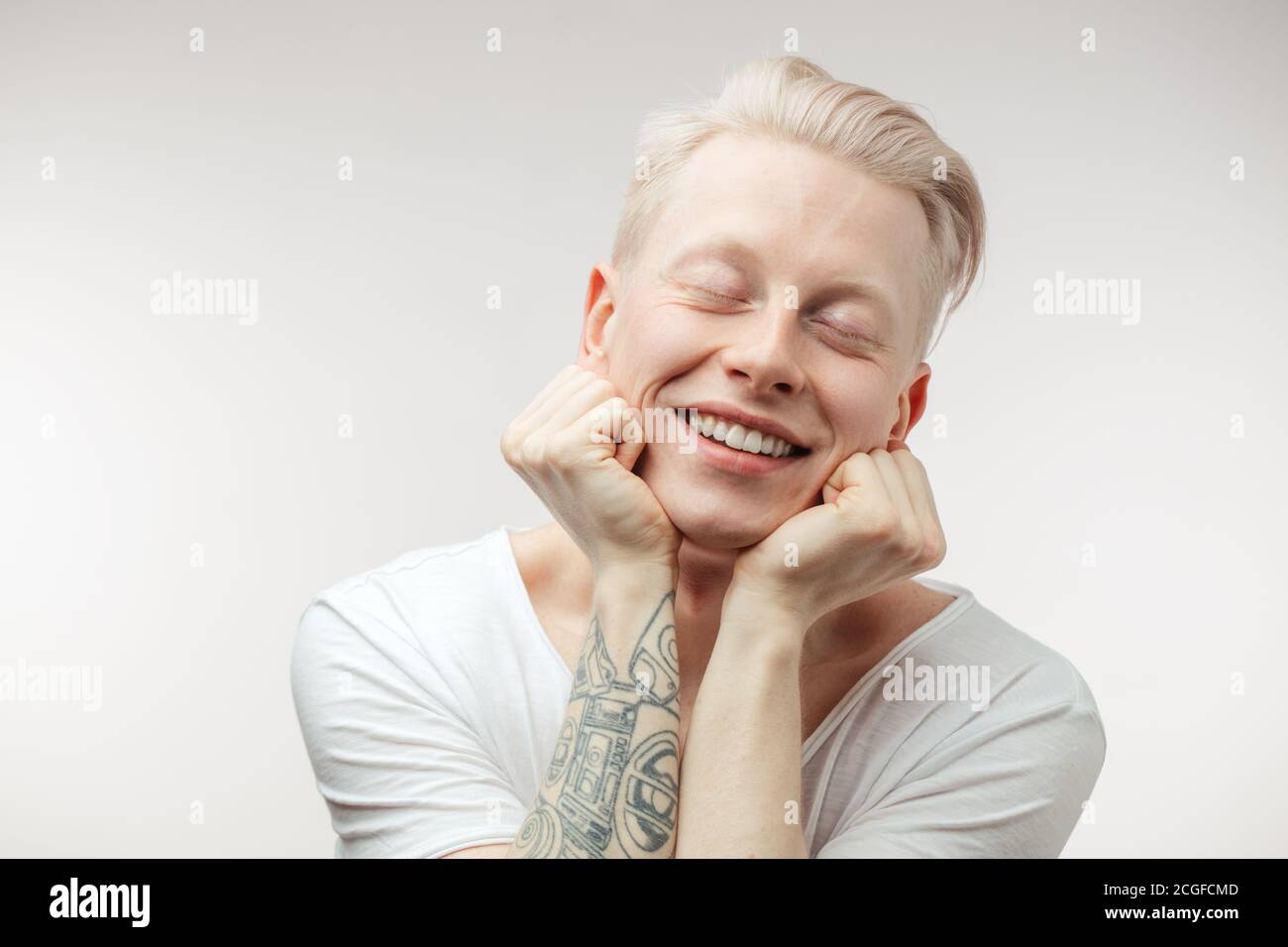 Hipster ragazzo appoggiandosi su mani tatuate che hanno un'espressione allegra e felice alla ricerca di . Emozioni positive Foto Stock