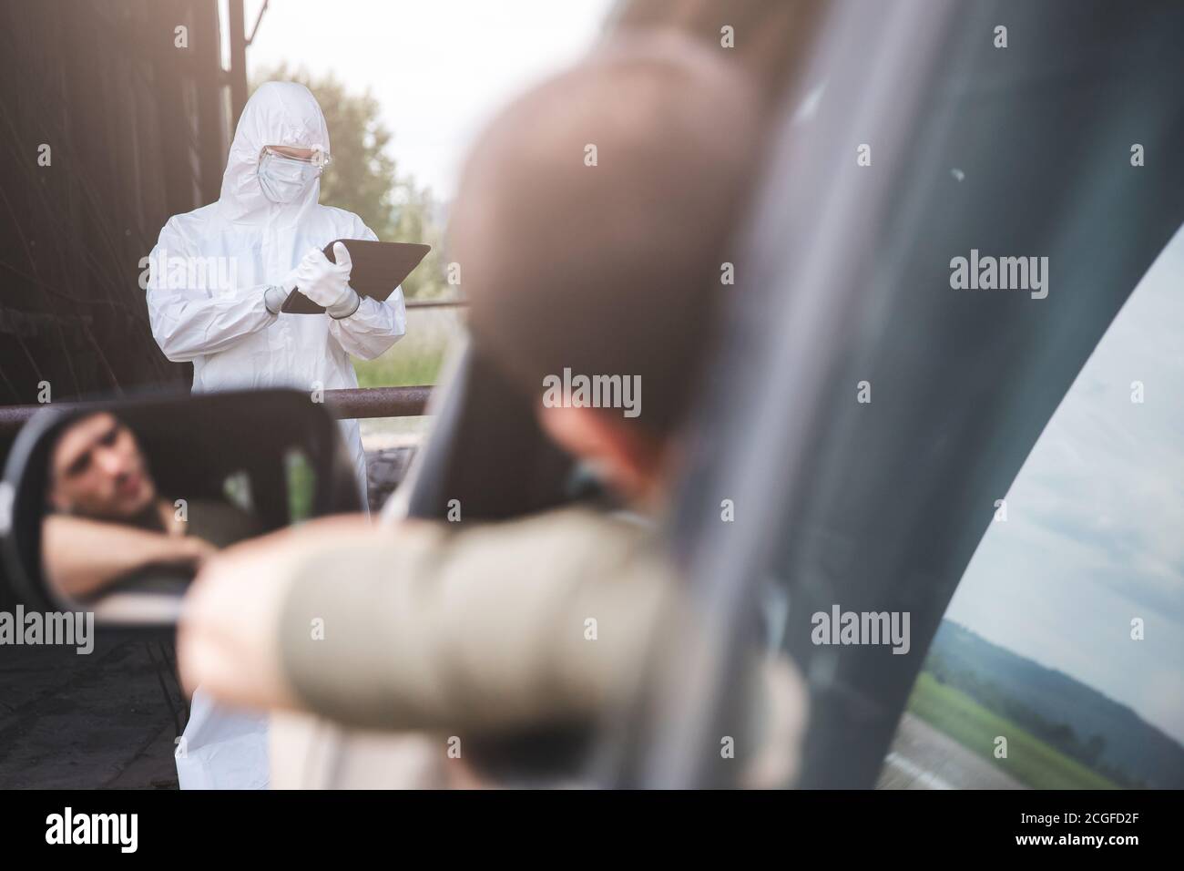 Controllando i passeggeri e il conducente per il virus, l'uomo in tuta biologica scrive i dati su tablet, numero di auto e percorso di viaggio. Concept Life after pandemic Foto Stock