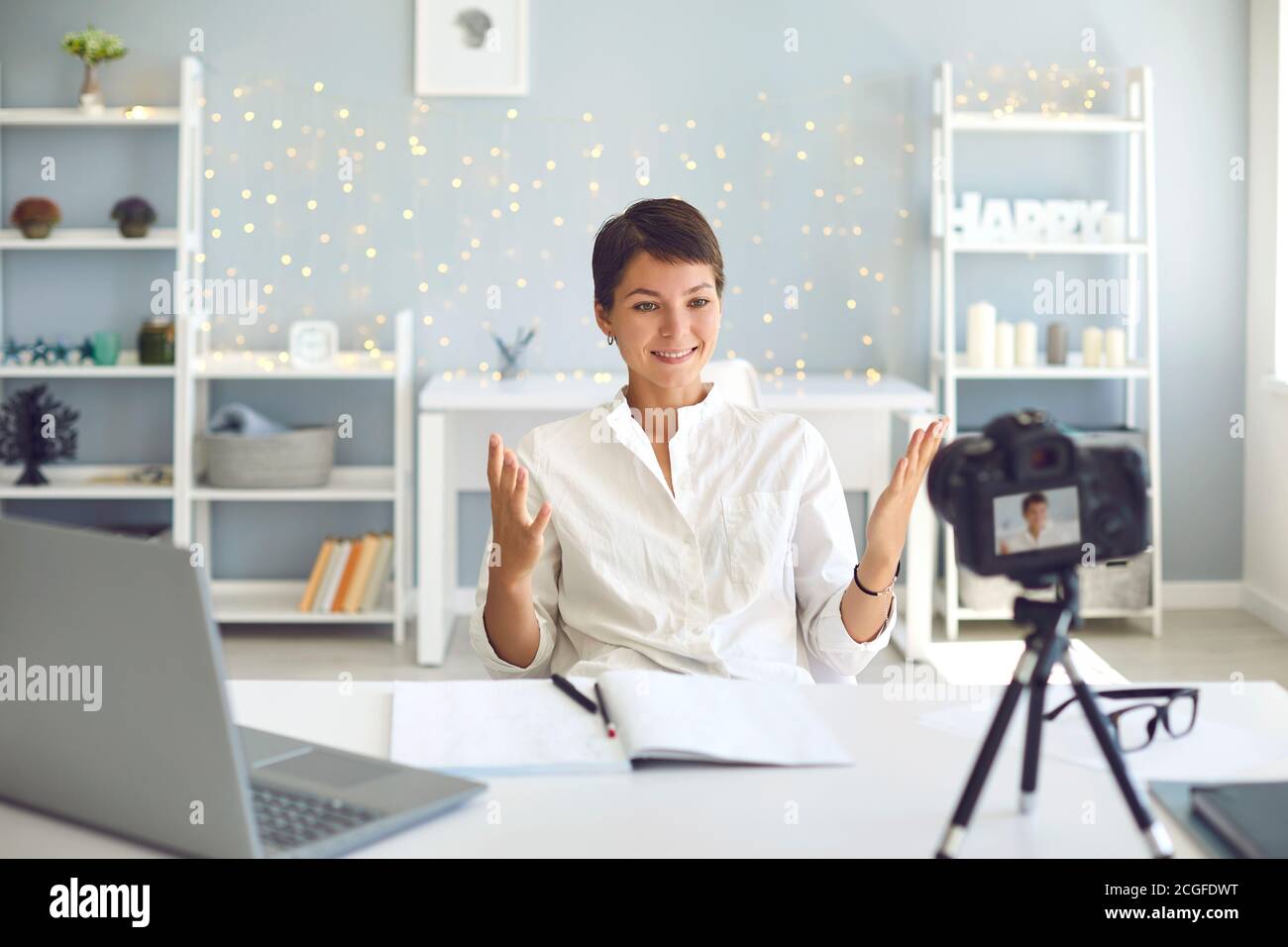 Allegro vlogger femminile che registra un video su telecamera seduto a. la sua scrivania in ufficio a casa Foto Stock