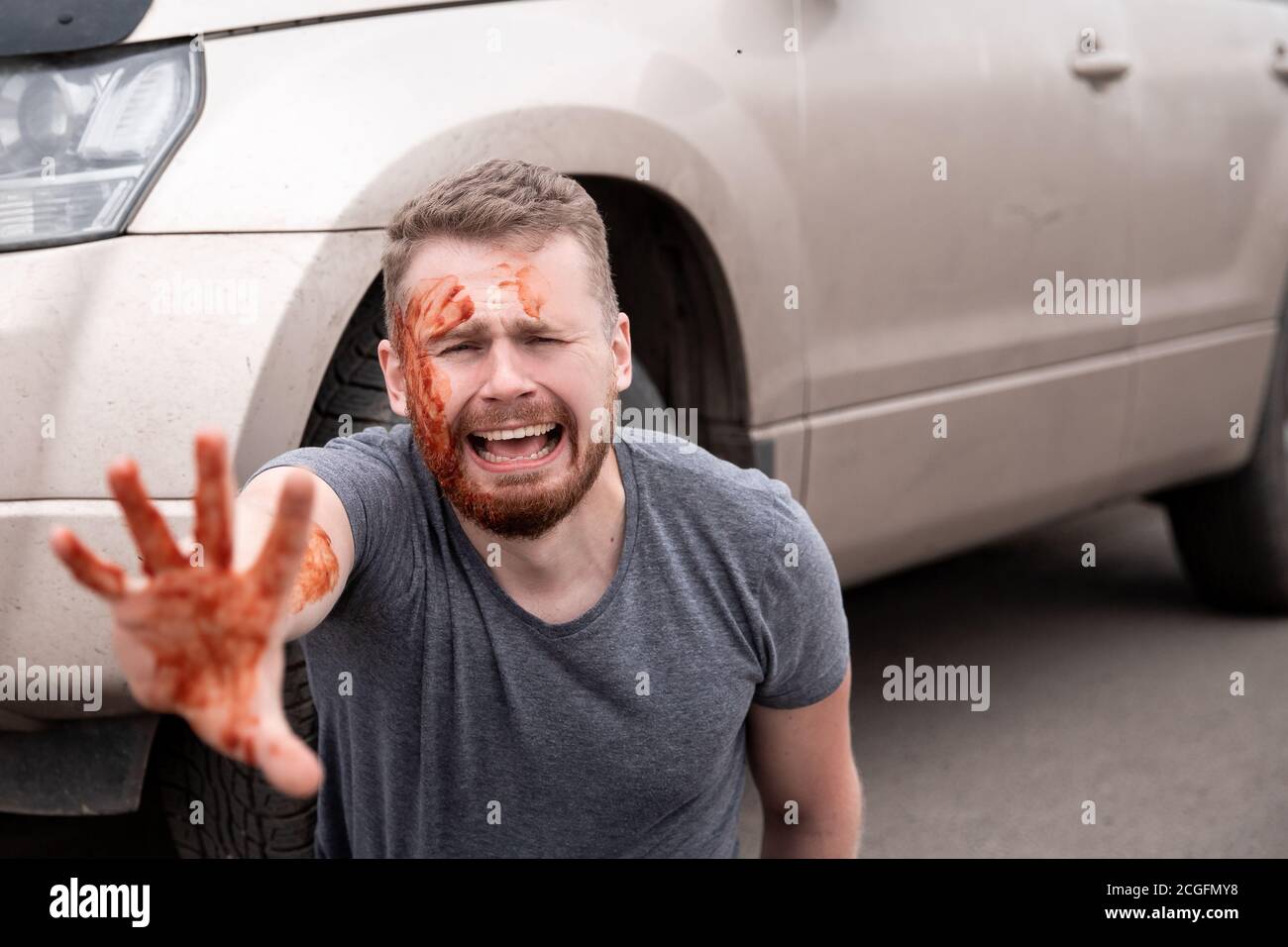 Incidente d'auto, l'uomo si siede con testa sanguinosa vicino ruota, urlando e piangendo Foto Stock