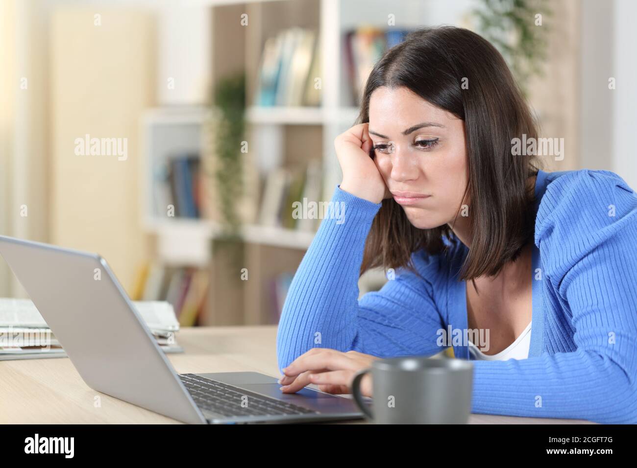 Donna annoiata che controlla i contenuti online del notebook seduto su una scrivania a casa Foto Stock