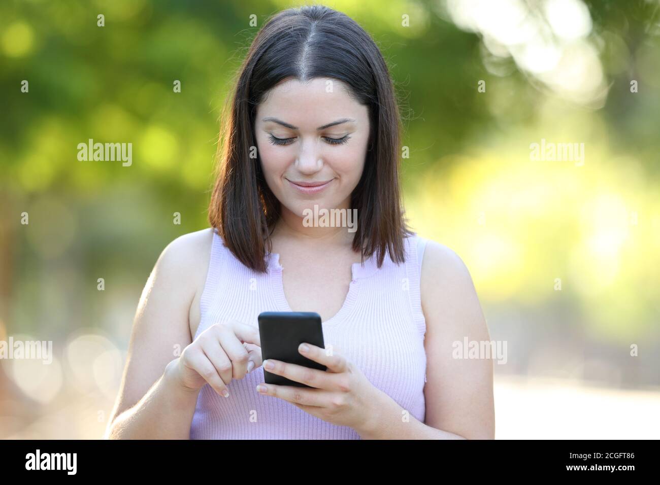 Vista frontale ritratto di una donna seria che utilizza uno smartphone passeggiate in un parco Foto Stock
