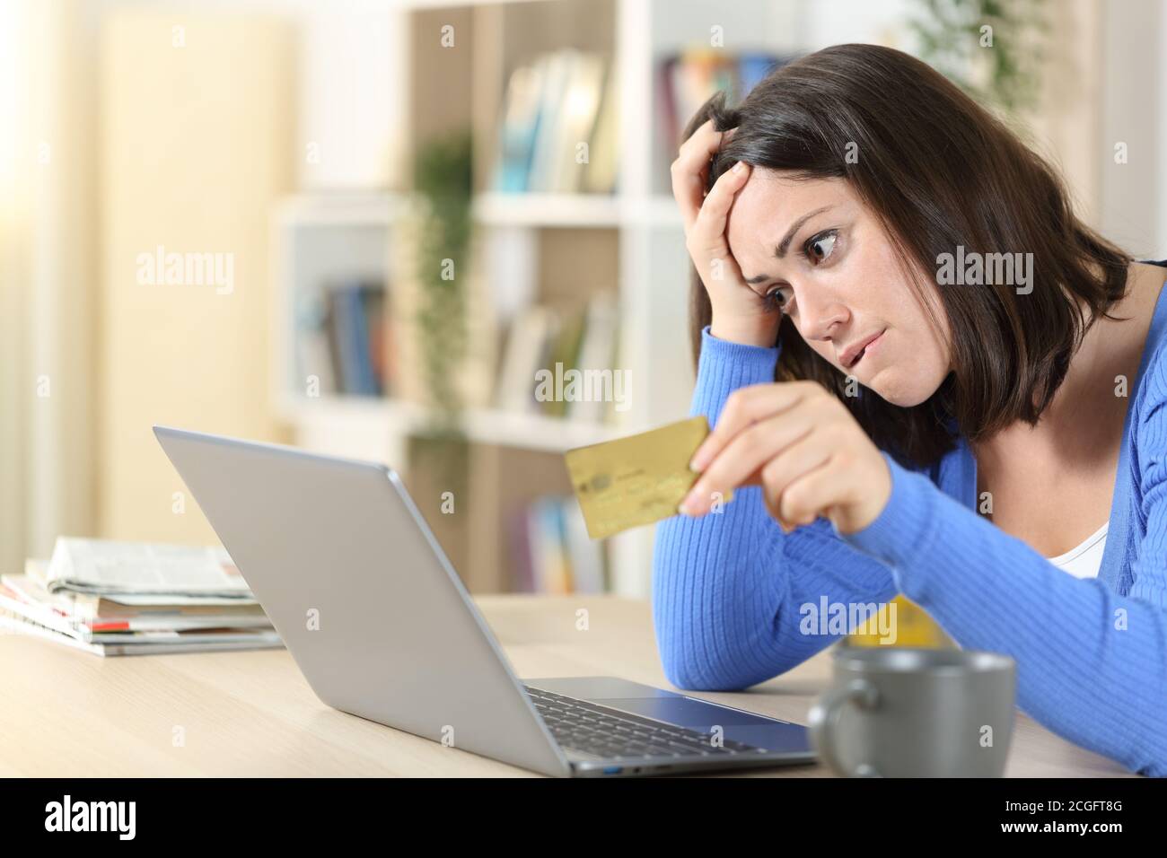 Donna preoccupata lamentando l'acquisto in linea con la carta di credito ed il laptop su una scrivania a casa Foto Stock