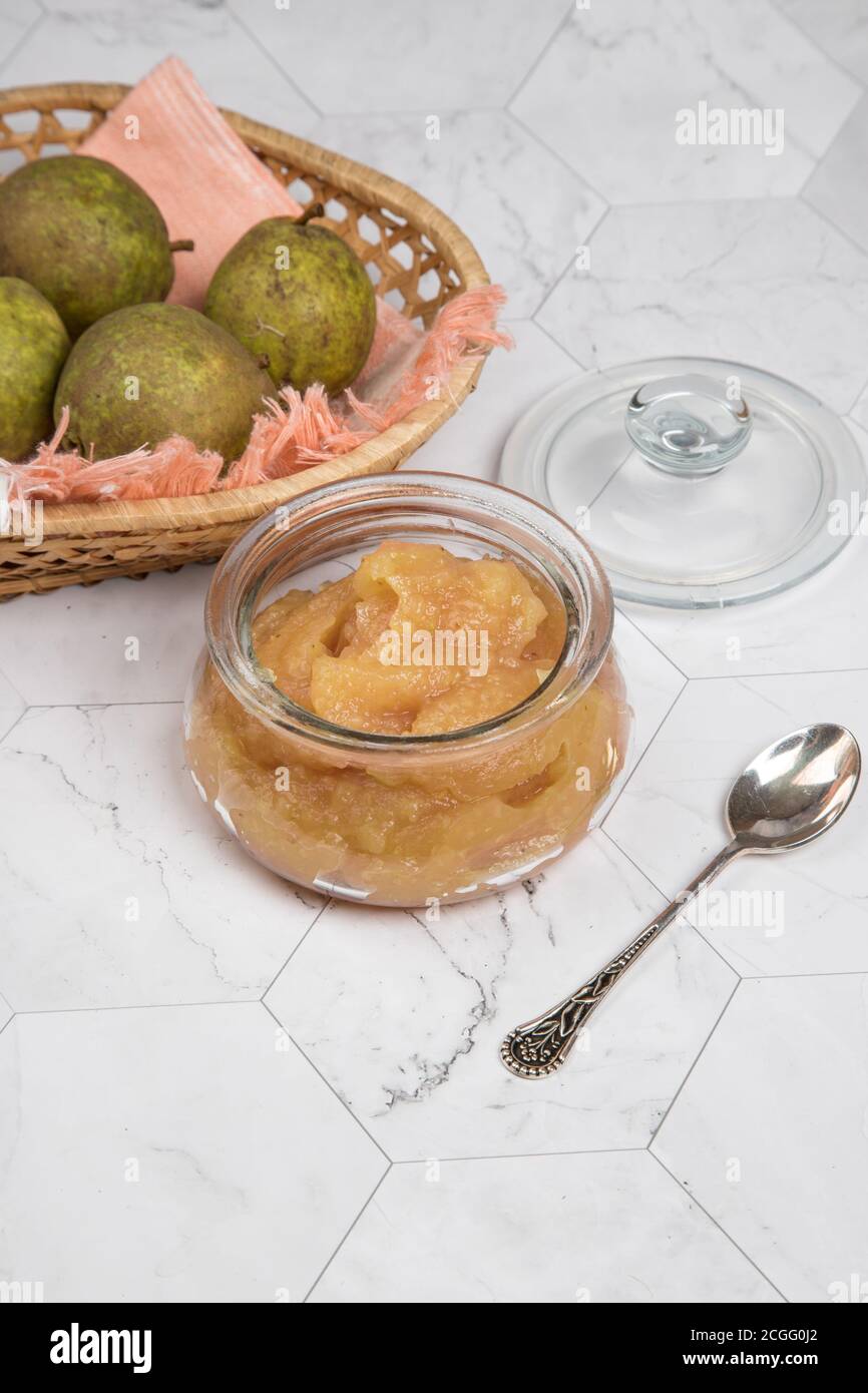 Vaso di vetro con purè di pere e pere fresche in un piatto di vimini su sfondo chiaro . Orientamento verticale. Foto Stock