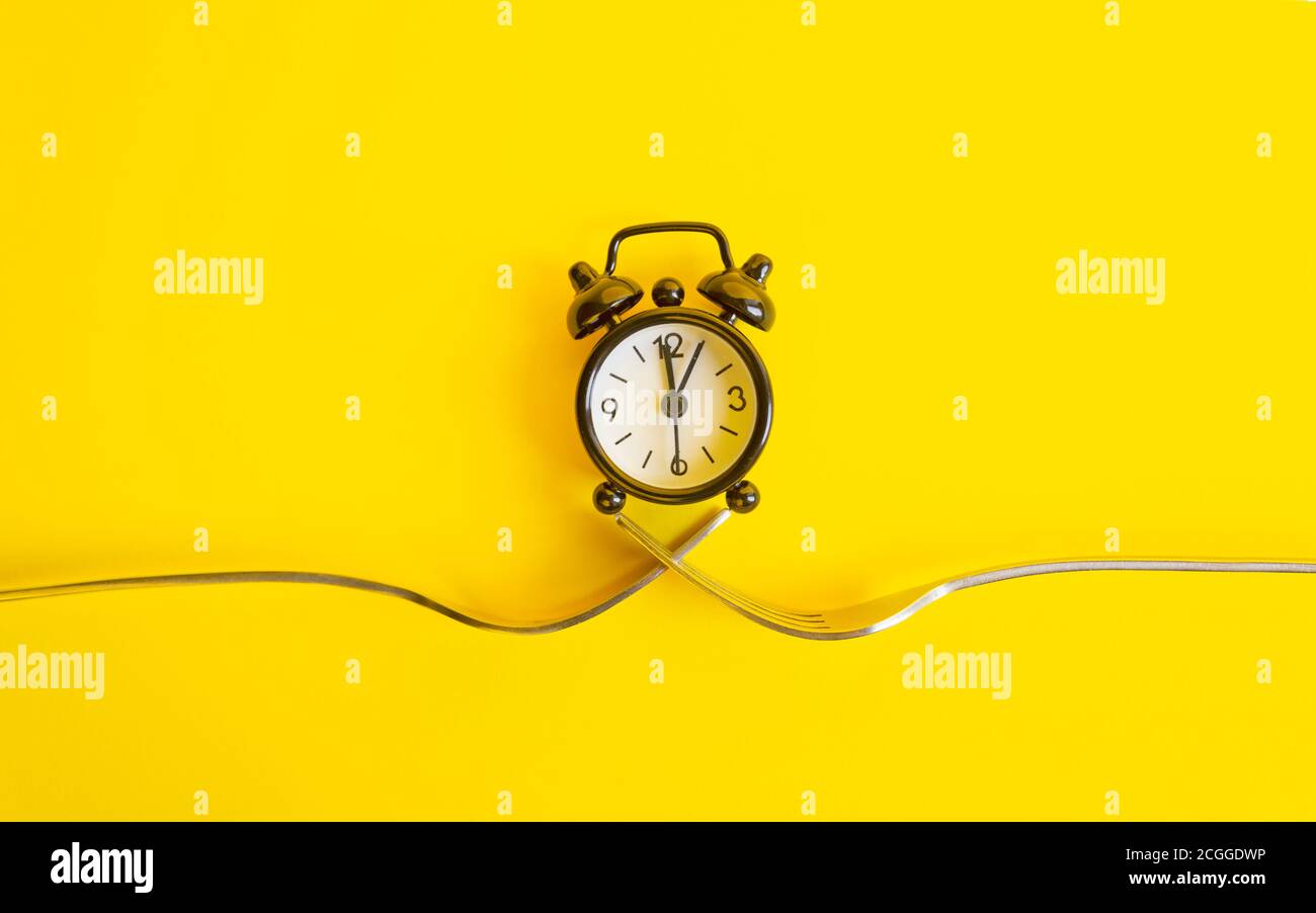 Orologio nero su sfondo giallo. Sveglia su due forcelle, trend Concept Time . Foto Stock