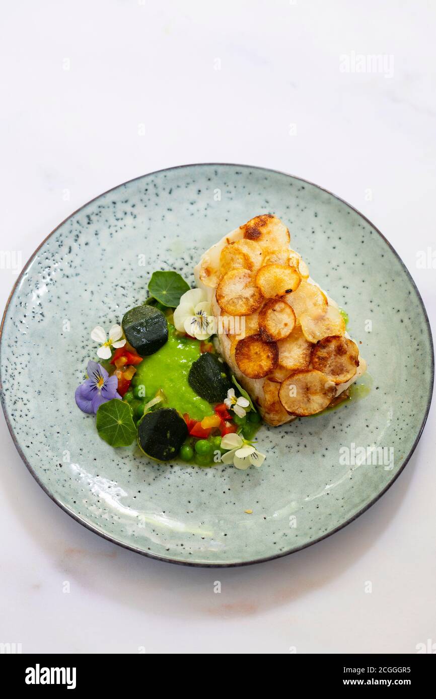 Filetto di pesce bianco con scala di patate, purea di piselli e verdure estive Foto Stock