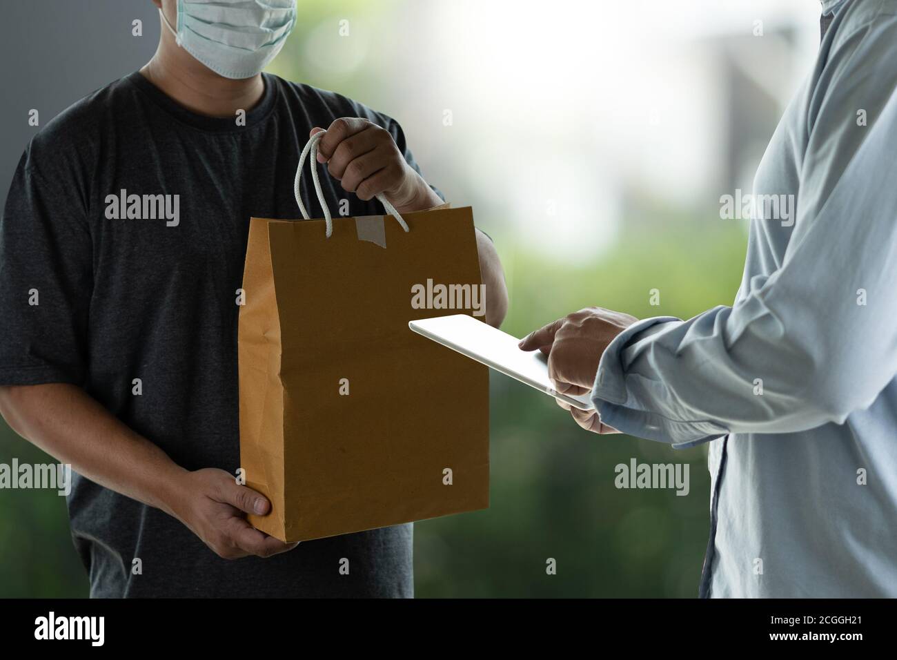 Addetto alla consegna che tiene scatole di cartone e accetta l'addetto alla consegna maschera protettiva Foto Stock