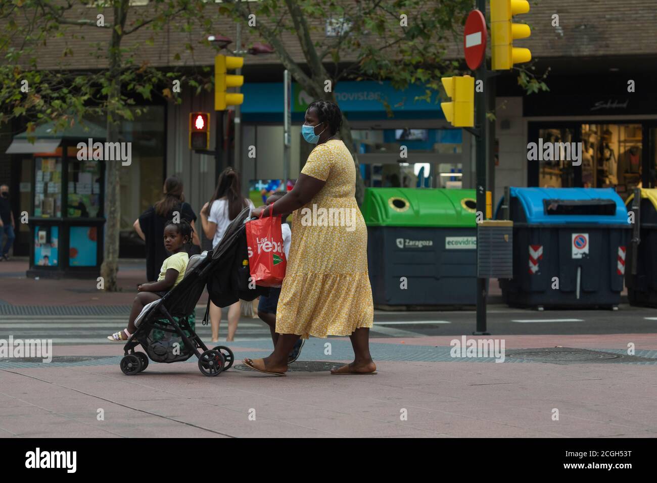 Saragozza, Spagna - 18 agosto 2020: Una donna immigrata nera, con maschere facciali, a causa della pandemia del coronavirus, spinge un passeggino con il suo bambino nel Foto Stock