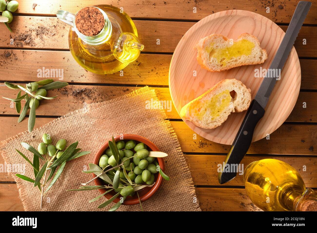 Fette di pane con olio su tavola di legno in campagna con contenitore pieno di olio e olive crude della vendemmia. Vista dall'alto. Foto Stock