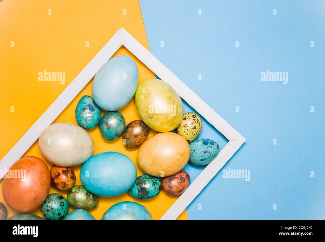 Painted Pasqua uova grandi e piccole su sfondo blu e giallo, cornice di legno bianco accanto ad esso . Spazio libero per il testo. Buona Pasqua! Foto Stock