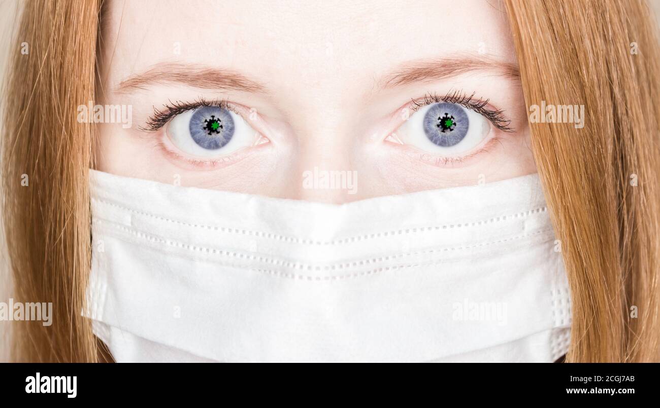 Primo piano del viso di una donna in una maschera medica o chirurgica. Il virus si riflette negli occhi . Il concetto di paura pandemica, COVID-19. Foto Stock