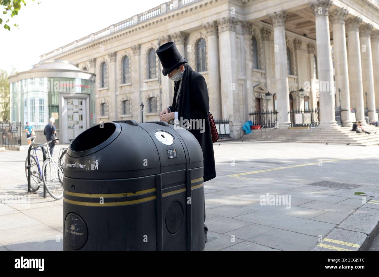 Londra, Inghilterra, Regno Unito. Uomo che indossa un cappello stovepipe che mette qualcosa in un bidone della lettiera, posto di San Martino Foto Stock